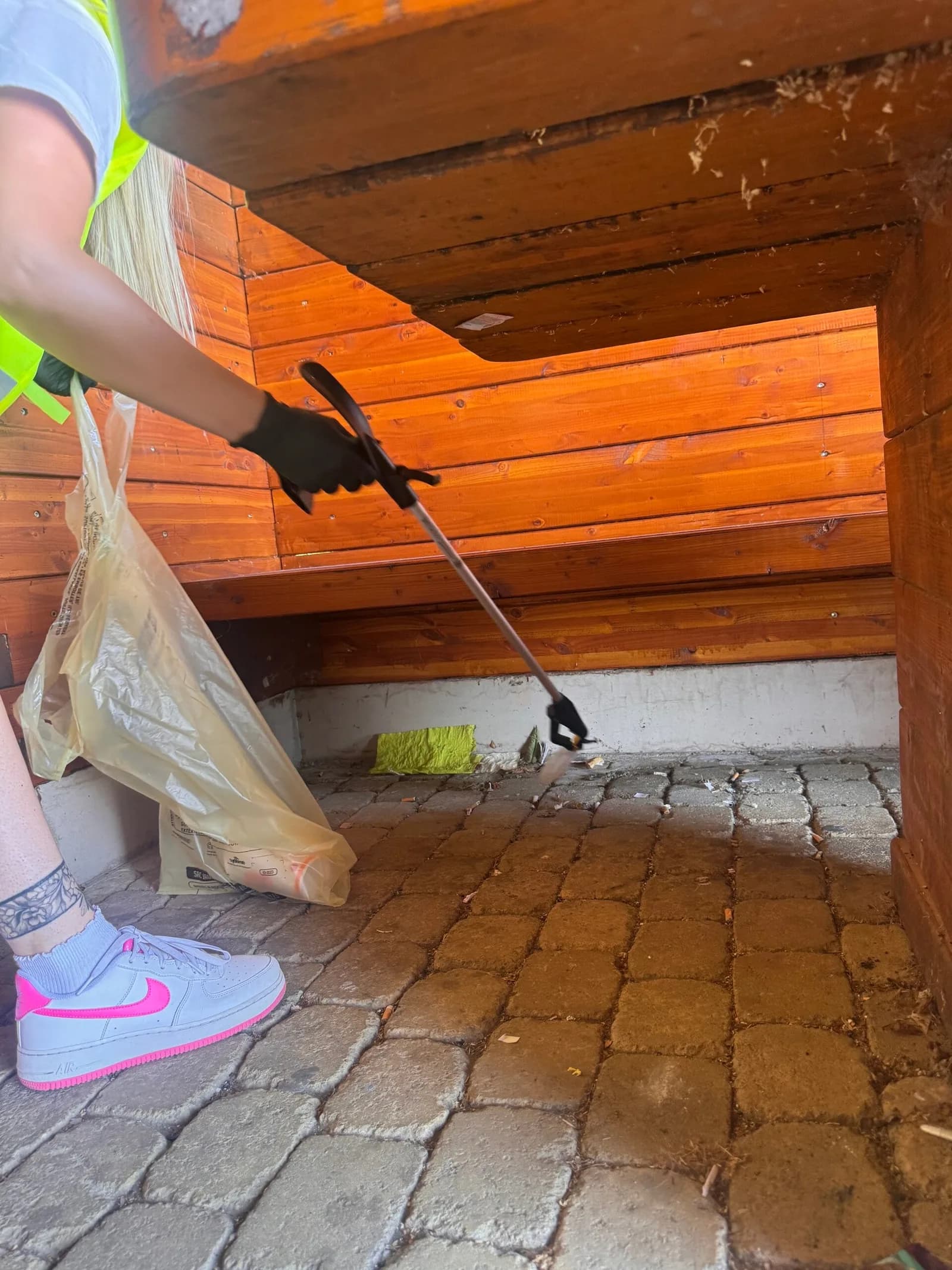 Une personne en gilet jaune ramasse des déchets avec une pince sous un abri en bois.