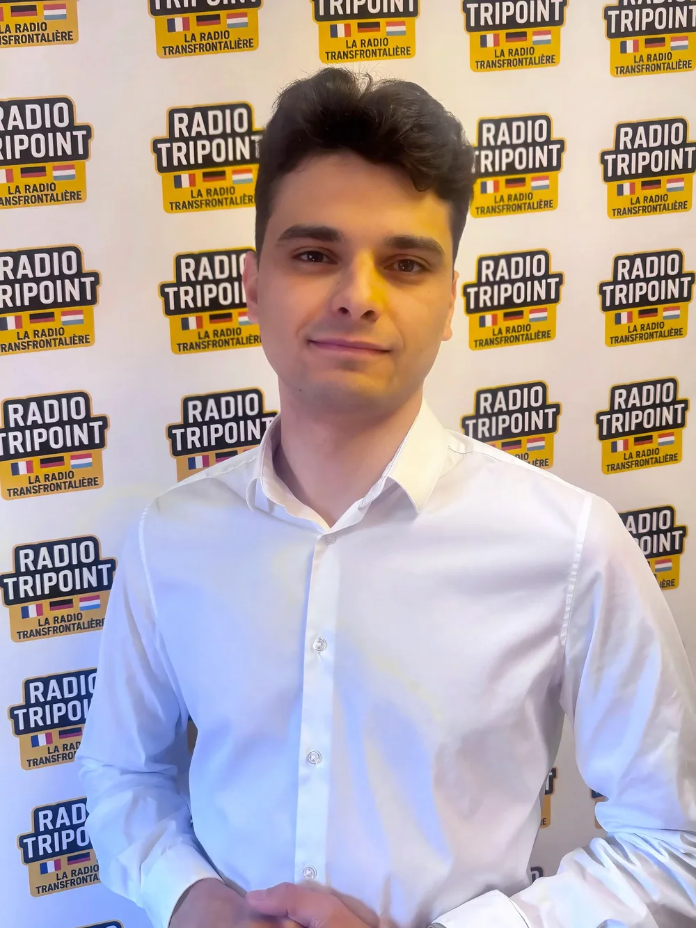 Martin Beziaud, en chemise blanche, devant le mur aux logos de Radio Tripoint.